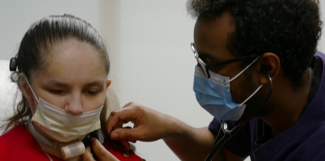 Photo of medical student examining a patient's neck with a stethoscope.