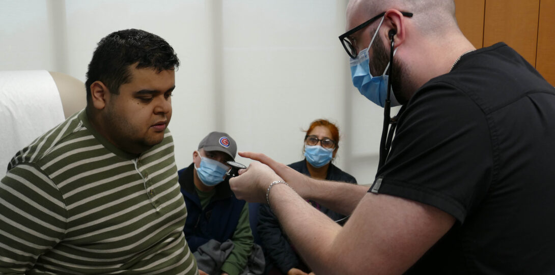 Photo of medical student explaining a stethoscope to a patient before examining him.